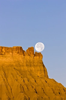 A full moon sets over Factory Butte at sunrise in the desert of southwestern Utah A full moon sets over Factory Butte at sunrise in the desert of southwestern Utah