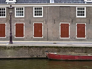 Netherlands, Amsterdam. Colorful red doors along the canal with a red boat