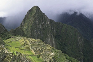 The ruins of the Machu Picchu citadel lie between the peak of Huayna Picchu and the The ruins of the Machu Picchu citadel lie between the peak of Huayna Picchu and the