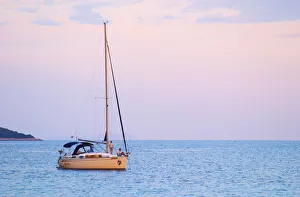 A sailing boat moored in the bay with two people on the deck off Korcula at sunset A sailing boat moored in the bay with two people on the deck off Korcula at sunset