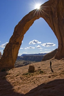 USA, Utah. A female hiker dwarfed by the Corona Arch near Moab. (MR) USA, Utah. A female hiker dwarfed by the Corona Arch near Moab. (MR)