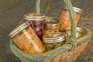 Wicker basket of home canned foods (peaches, olives and cherries) on a granite countertop Wicker basket of home canned foods (peaches, olives and cherries) on a granite countertop
