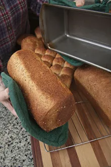 Woman removing loaf of just baked multigrain bread from bread pan. (MR) Woman removing loaf of just baked multigrain bread from bread pan. (MR)