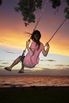 Young Girl on Rope Swing under Pohutukawa Tree at Sunset, Thames, Coromandel, North Island Young Girl on Rope Swing under Pohutukawa Tree at Sunset, Thames, Coromandel, North Island