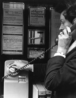 Woman dialling 999 in a public telephone box, London Woman dialling 999 in a public telephone box, London