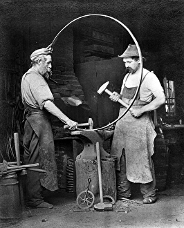 BLACKSMITHS, c1903. Two blacksmiths making a metal hoop, possibly for a wagon wheel BLACKSMITHS, c1903. Two blacksmiths making a metal hoop, possibly for a wagon wheel