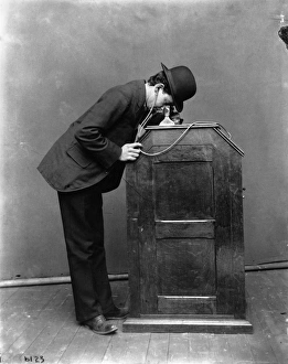 KINETOPHONE, 1895. A man looking into a Kinetophone, wearing earphones that connect KINETOPHONE, 1895. A man looking into a Kinetophone, wearing earphones that connect