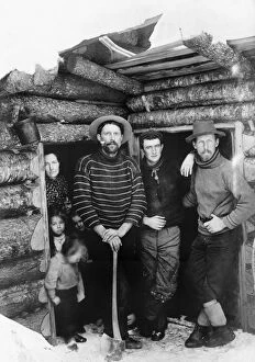 LOG CABIN, c1903. Three men, a woman and four children standing in the doorway of a log cabin