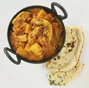 Aloo Gosht, chunky meat curry in deep bowl with two handles, pieces of bread, overhead view