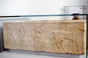 Ancient Greek warrior stepping into his chariot. Behind him are two hoplites carrying Ancient Greek warrior stepping into his chariot. Behind him are two hoplites carrying