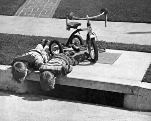<b class=qtipBold><figcaption>Two Boys Peer In Storm Drain</figcaption></b><br>Long Beach, California: March 15, 1957. Two boys park their tricycle and peer down a storm drain, wondering where their penny went.<br><em>© A</em> Two Boys Peer In Storm Drain