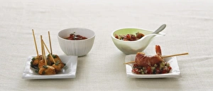 Chicken pieces on skewers on small square plate and bowl of sauce Chicken pieces on skewers on small square plate and bowl of sauce