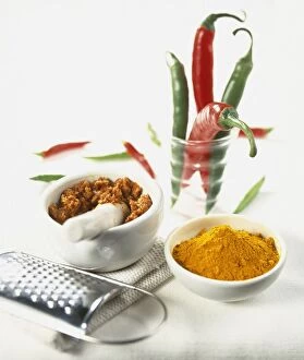 Ground turmeric, crushed spices in mortar, and whole green and red chilli peppers in glass