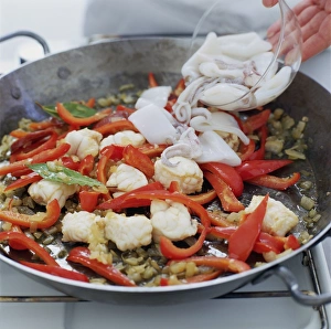 Making paella, adding bowl of squid to pan of onion, garlic, red pepper and monkfish Making paella, adding bowl of squid to pan of onion, garlic, red pepper and monkfish