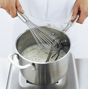 Metal whisk being used to stir milk and vanilla pods in saucepan, high angle view Metal whisk being used to stir milk and vanilla pods in saucepan, high angle view