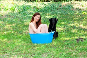 A Naked Woman Smiling in the Garden in a Bucket Blue with a Black Dog A Naked Woman Smiling in the Garden in a Bucket Blue with a Black Dog