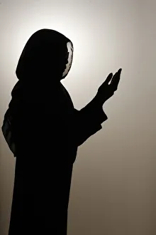 Silhouette of muslim woman in abaya prays with her hands up in air Silhouette of muslim woman in abaya prays with her hands up in air