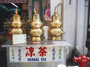 Singapore, Chinatown, Temple Street, decorative herbal tea dispensers, gold coloured metal decorated with Chinese script and dragons, lid loosely placed on central dispenser, standing on metal box, shop in background Singapore, Chinatown, Temple Street, decorative herbal tea dispensers, gold coloured metal decorated with Chinese script and dragons, lid loosely placed on central dispenser, standing on metal box, shop in background
