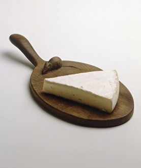 Slice of Brie on circular wooden chopping board with handle, elevated view Slice of Brie on circular wooden chopping board with handle, elevated view