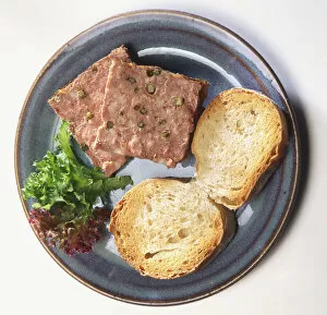 Two square slices of port-flavoured pate seasoned with green peppercorns, served on blue plate with two slices of