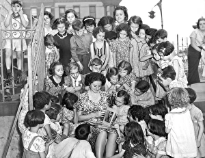<b class=qtipBold><figcaption>Summertime Playground Reading</figcaption></b><br>New York, New York: c. 1938. A playground instructor reads to an attentive gathering of children during the summer vacation from school.<br><em>© Underwood Archives/UIG</em> Summertime Playground Reading