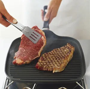 Using tongs to turn over steaks being char-grilled on a ridged, cast-iron grill pan Using tongs to turn over steaks being char-grilled on a ridged, cast-iron grill pan
