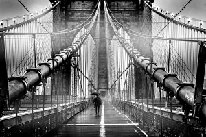 A lone man with umbrella walks along a foggy Brooklyn Bridge at dusk in black and white A lone man with umbrella walks along a foggy Brooklyn Bridge at dusk in black and white