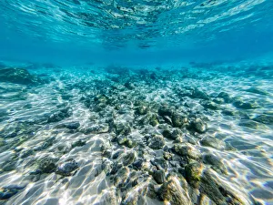 Underneath a wave in the clear ocean waters looking at rocks and shells on the ocean floor Underneath a wave in the clear ocean waters looking at rocks and shells on the ocean floor