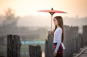 Beautiful woman holding traditional red umbrella and walking on U Bein Bridge, Myanmar Beautiful woman holding traditional red umbrella and walking on U Bein Bridge, Myanmar