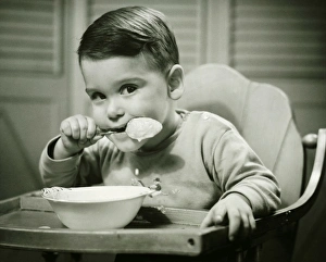 Boy (4-5) sitting in high chair, eating porridge, (B&W), portrait Boy (4-5) sitting in high chair, eating porridge, (B&W), portrait