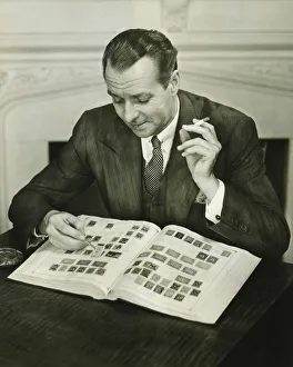 Businessman sitting at small table, with stamp album, (B&W) Businessman sitting at small table, with stamp album, (B&W)