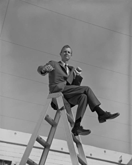 Legs Crossed At Knee Gallery: Businessman sitting on top of step ladder, portrait