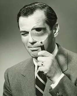 Businessman in full suit in studio looking through magnifying glass, (B&W), portrait Businessman in full suit in studio looking through magnifying glass, (B&W), portrait