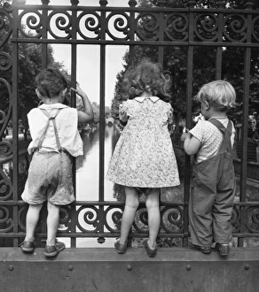 Three children peer through the fence on a bridge over one of Londons many canals Three children peer through the fence on a bridge over one of Londons many canals