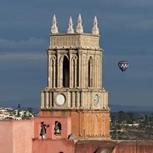 Clock tower and bells of the parish church with a hot air balloon flight in the distance Clock tower and bells of the parish church with a hot air balloon flight in the distance