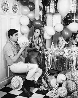 Couple blowing up balloons in kitchen for party, (B&W) Couple blowing up balloons in kitchen for party, (B&W)