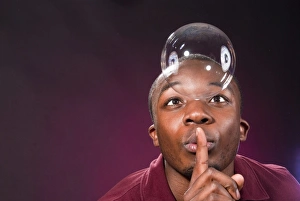 Dark-skinned young man with soap-bubble, making a gesture of silence Dark-skinned young man with soap-bubble, making a gesture of silence