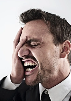 Desperate young man wearing a suit covering his face with his hand, screaming Desperate young man wearing a suit covering his face with his hand, screaming