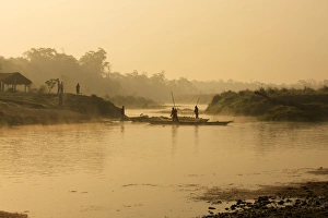 Dugout canoe with punting ferryman crossing a small river early in the morning Dugout canoe with punting ferryman crossing a small river early in the morning