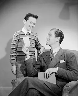 Legs Crossed At Knee Gallery: Father showing card to son (10-11 years)