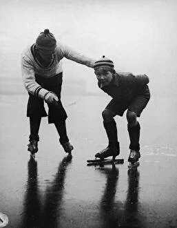Father teaching son (10-12) to ice skate on frozen lake (B&W)