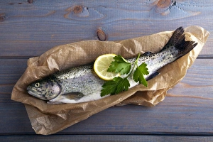Fresh brook trout in baking paper on a wooden surface Fresh brook trout in baking paper on a wooden surface