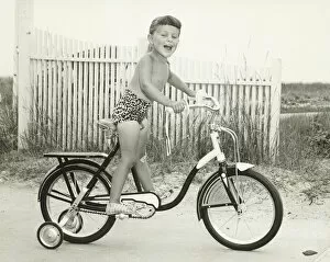 Images Dated 5th May 2006: Girl (6-7) riding bicycle with side wheels, (B&W)