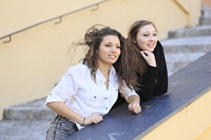 Two girlfriends, teenagers, leaning on the railing of a staircase Two girlfriends, teenagers, leaning on the railing of a staircase