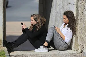 Two girlfriends, teenagers, sitting on the floor, leaning against a wall Two girlfriends, teenagers, sitting on the floor, leaning against a wall