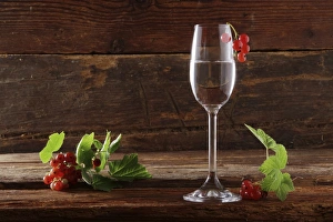 A glass of red currant schnapps with red currants (Ribes rubrum) on wooden background A glass of red currant schnapps with red currants (Ribes rubrum) on wooden background