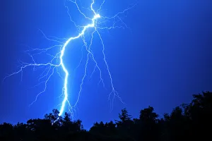 <b class=qtipBold><figcaption>Lightning in a Thunderstorm</figcaption></b><br>Massive fork lightning strike at night. Forked lightning bolt from the sky to the ground with trees silhouetted in the bottom of the picture and a blue night sky behind<br><em>© RMR Rayner 2017</em> Lightning in a Thunderstorm