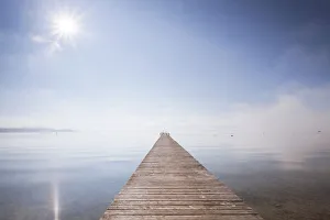 Very long jetty on Chiemsee Lake with high fog and sun near Seebruck, Bavaria, Germany Very long jetty on Chiemsee Lake with high fog and sun near Seebruck, Bavaria, Germany