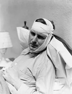 Man In Bed With Bandage Around Head And Chin, Looks In Pain From Mumps Man In Bed With Bandage Around Head And Chin, Looks In Pain From Mumps