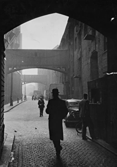 A man in a bowler hat walking under the arches on the cobbled Wapping High Street, London A man in a bowler hat walking under the arches on the cobbled Wapping High Street, London